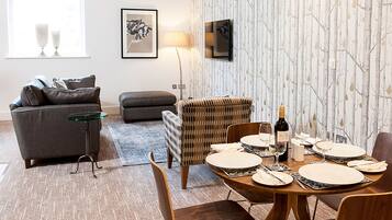 A modern living room with a dining area, a sofa, a coffee table, and a TV mounted on the wall.