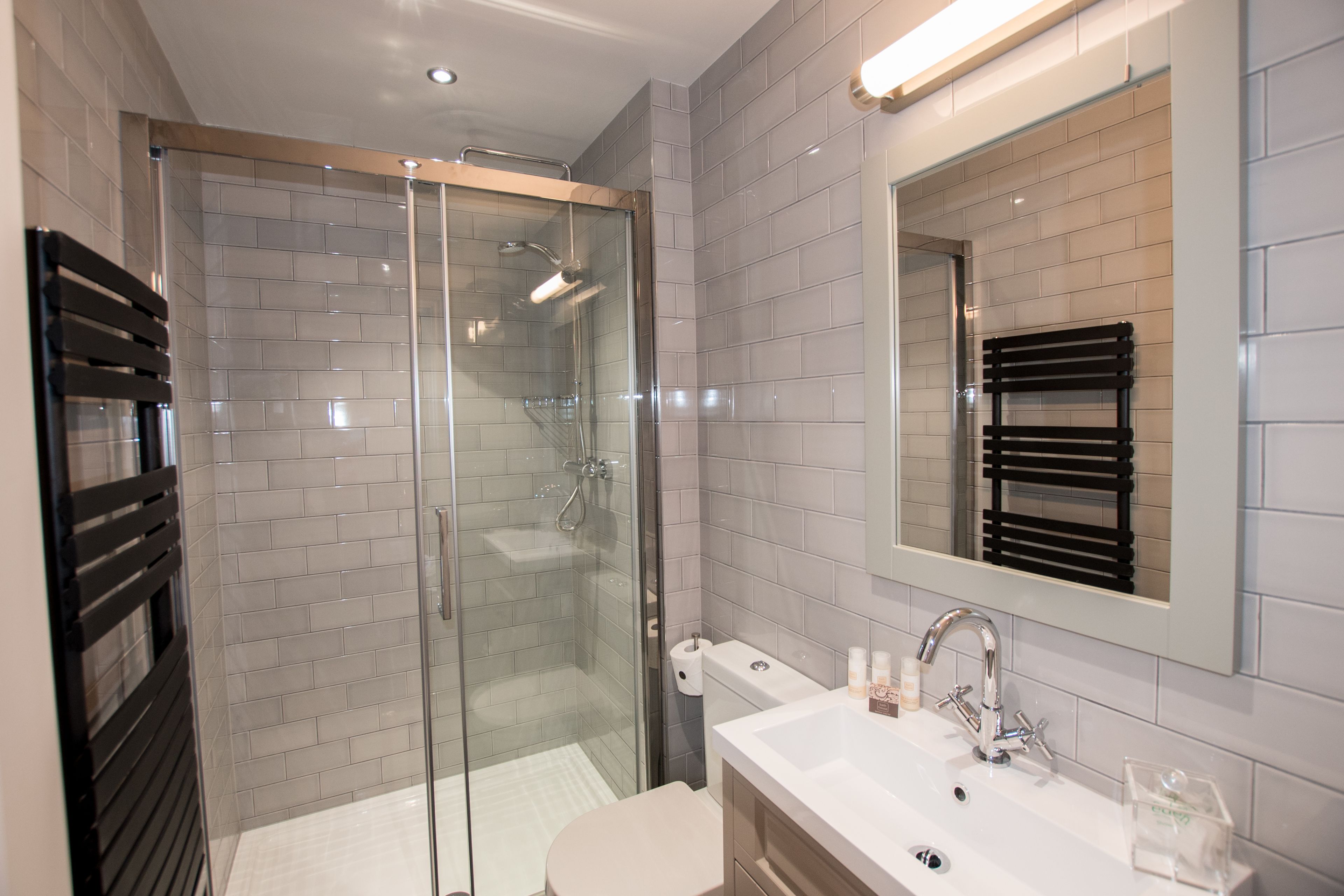 A modern bathroom with a glass-enclosed shower, a white sink with a mirror, and a towel rack.
