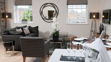 A modern living room with a sofa, armchair, dining table set for two, and a large mirror on the wall.