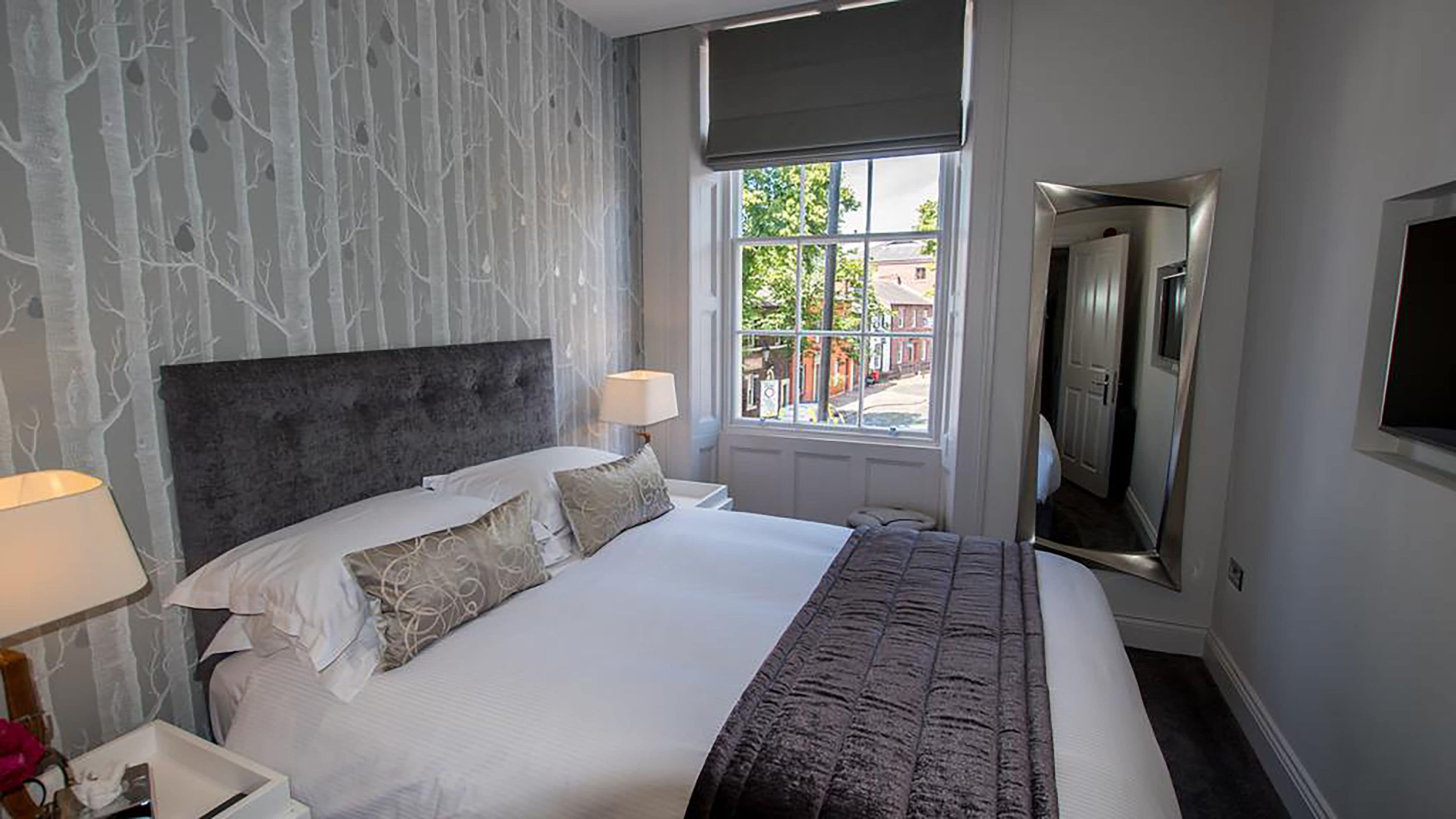 Habitación de hotel con una cama grande, cabecero, dos lámparas de noche, ventana con vistas al exterior y televisor de pantalla plana montado en la pared.