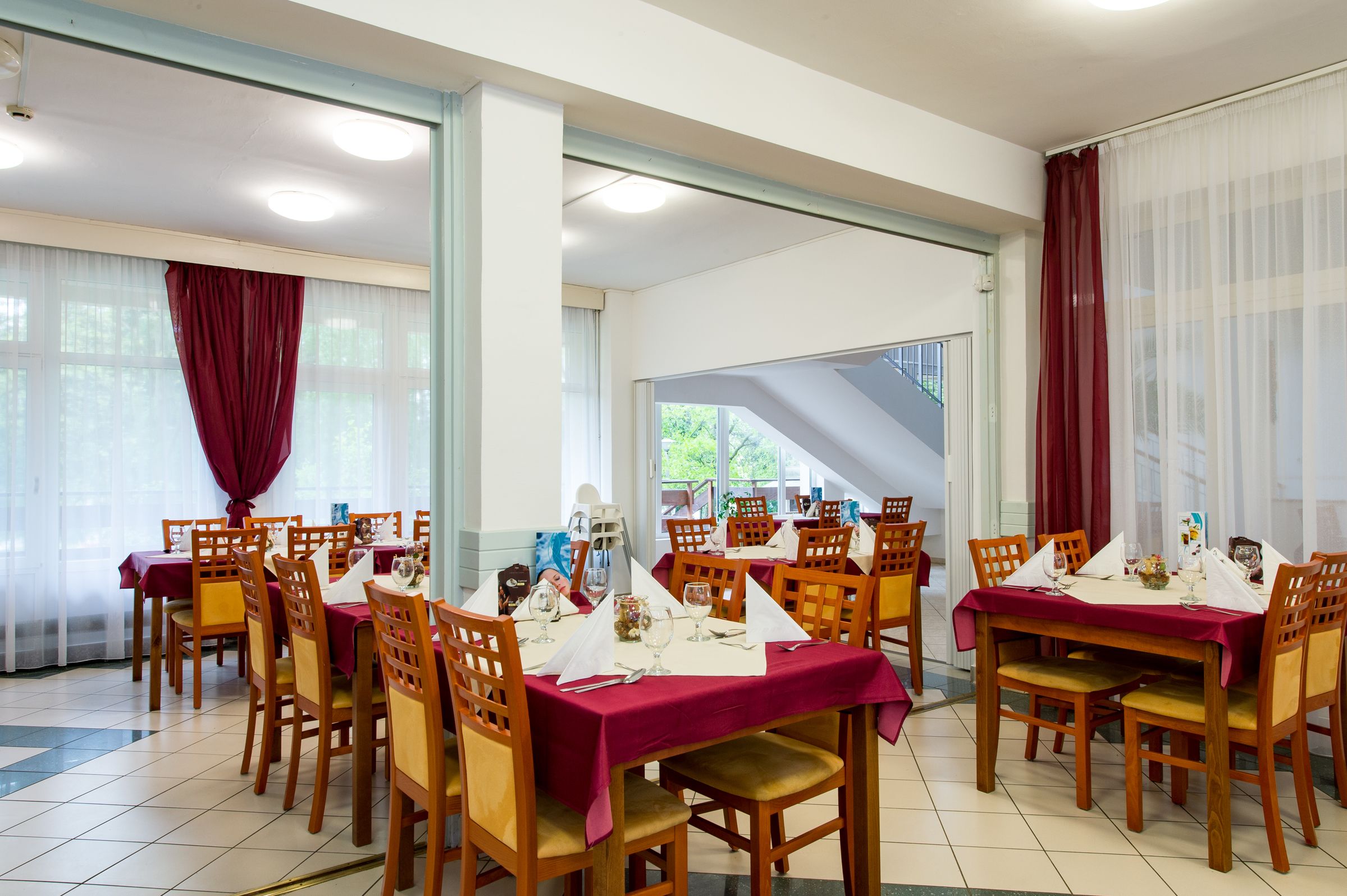 Un comedor con varias mesas dispuestas para comidas, sillas de madera y vistas al exterior a través de amplios ventanales.