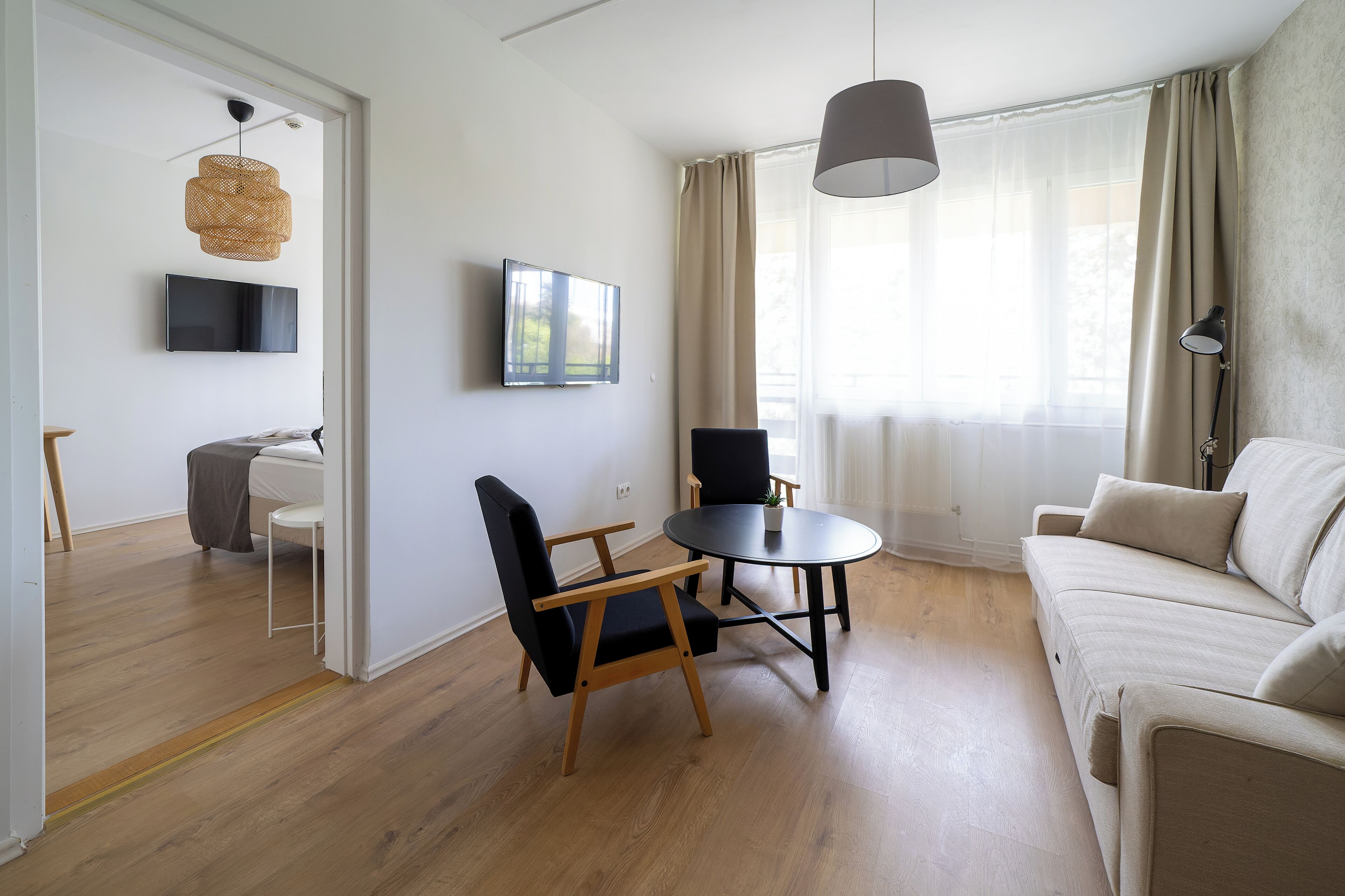 Una sala de estar moderna con un sofá, dos sillones, una mesa redonda, un televisor y un ventanal con cortinas.