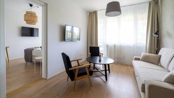 Una sala de estar moderna con un sofá, dos sillones, una mesa redonda, un televisor y un ventanal con cortinas.