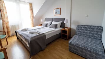 Una habitación de hotel con una cama, dos mesitas de noche, una silla, un sofá y una ventana con cortinas.
