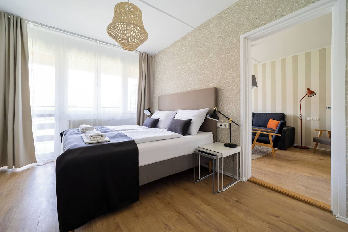 Une chambre d’hôtel moderne, dotée d’un grand lit, de tables de chevet, d’un bureau et offrant une vue sur la chambre voisine.