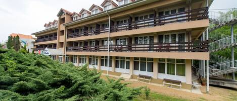 A multi-story hotel with balconies, a covered outdoor seating area, and a staircase leading to an upper level.