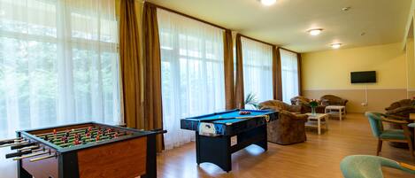 A room with a foosball table, pool table, and comfortable seating area with a television.