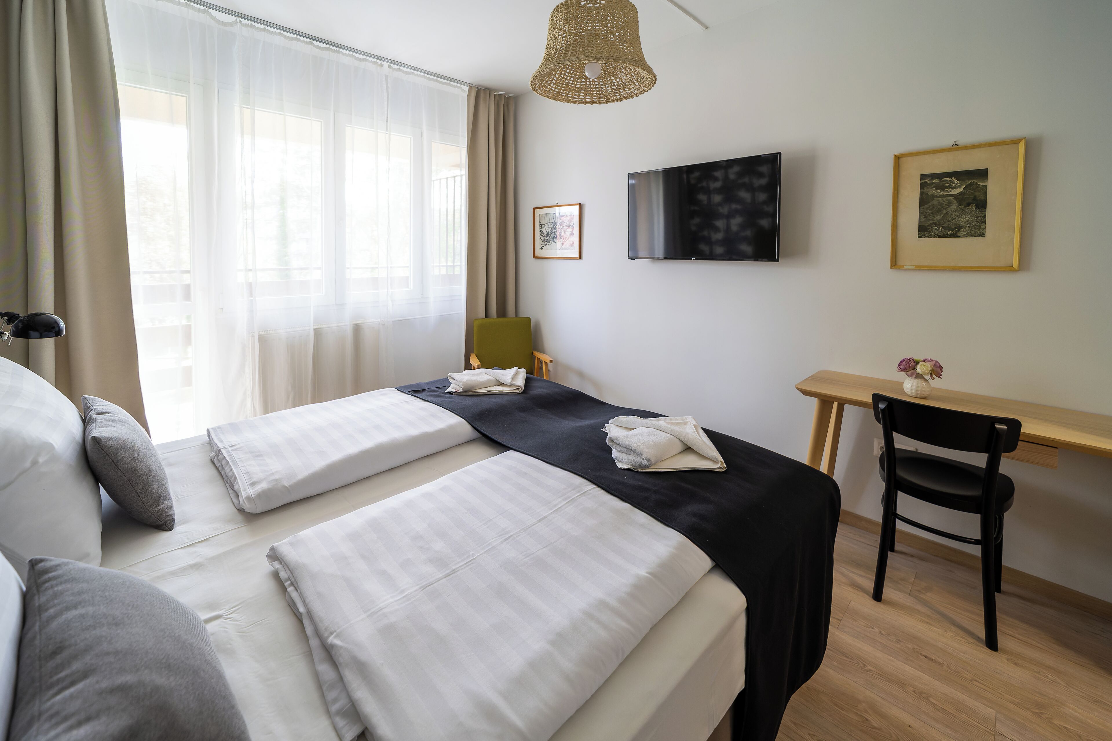 Ein Hotelzimmer mit zwei Betten, einem Schreibtisch, einem Stuhl, einem Fernseher und einem Fenster mit Vorhängen.