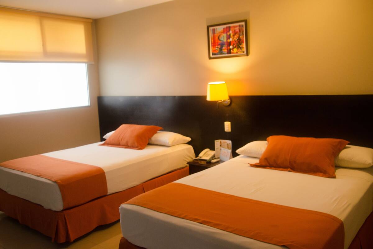 Dos camas individuales con ropa de cama naranja, una mesita de noche con lámpara y un cuadro en la pared.