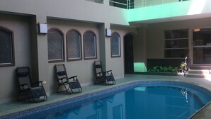 A swimming pool with lounge chairs, a multi-level building with balconies, and a clear sky. - Hotel Los Almendros (Manta)