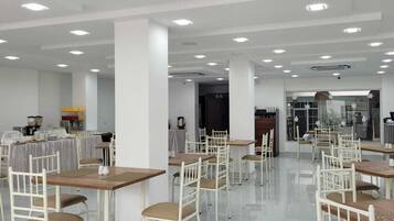 Un comedor amplio con varias mesas y sillas, una zona de cocina al fondo y un ventanal que proporciona luz natural.