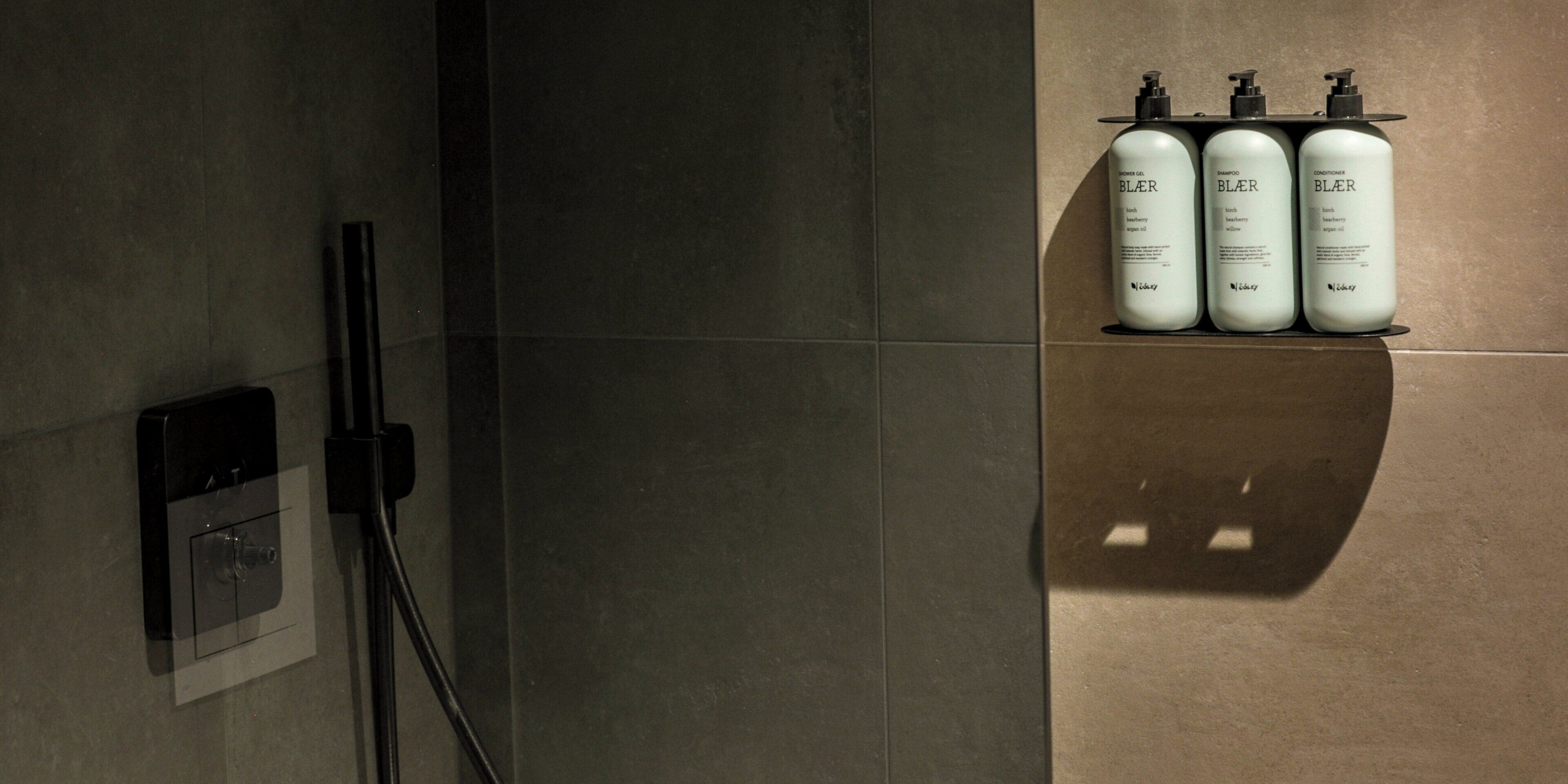 A bathroom with a shower, a towel rack, and three bottles of shampoo on a shelf.