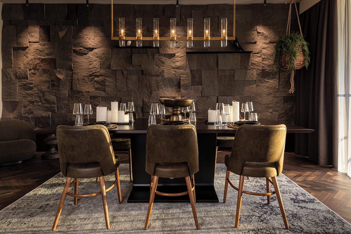 A modern dining area with a stone wall backdrop, a chandelier, and a central island with a bowl.
