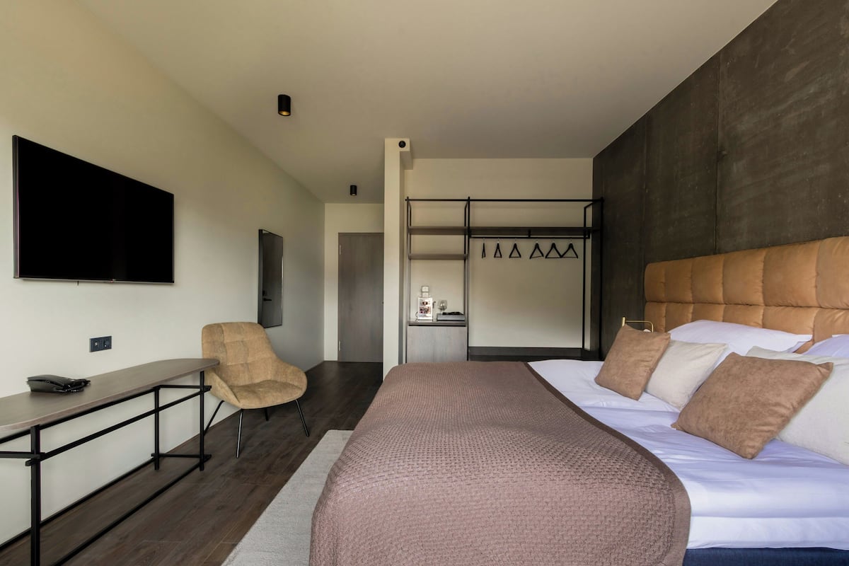 A modern hotel room with a large bed, a flat-screen TV, a desk, and a seating area.