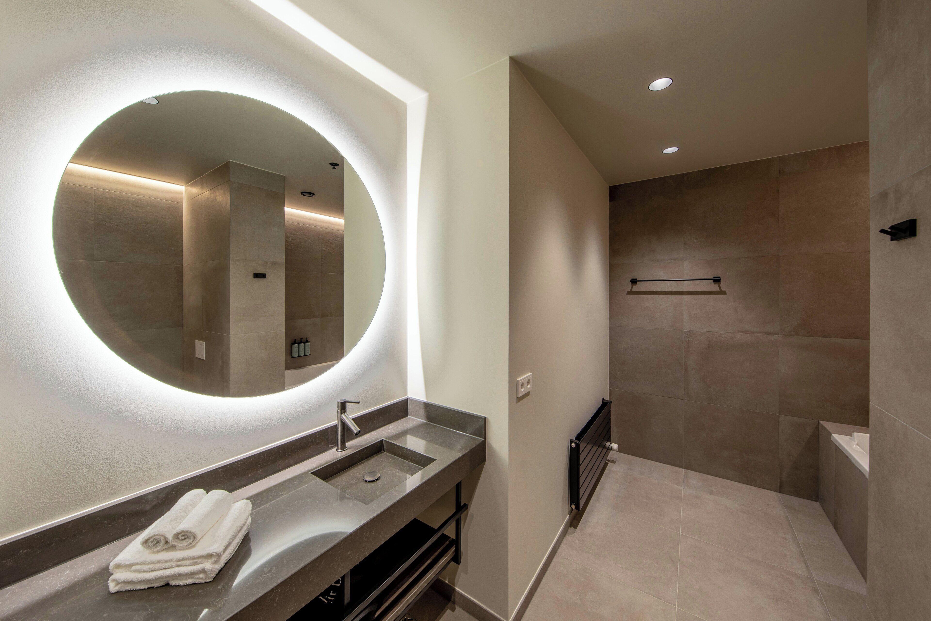 Un baño moderno con un espejo redondo, un lavamanos y una zona de ducha.