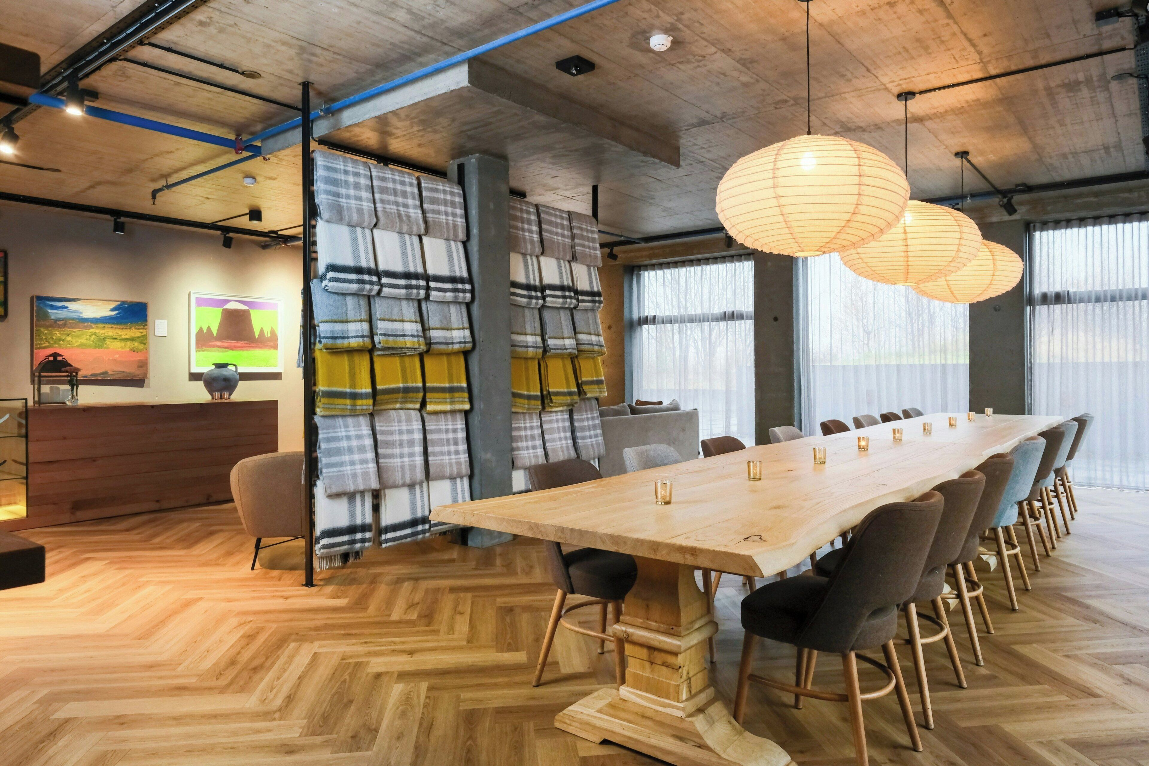 Un salón de conferencias con una larga mesa de madera, sillas, un sofá y un amplio ventanal.