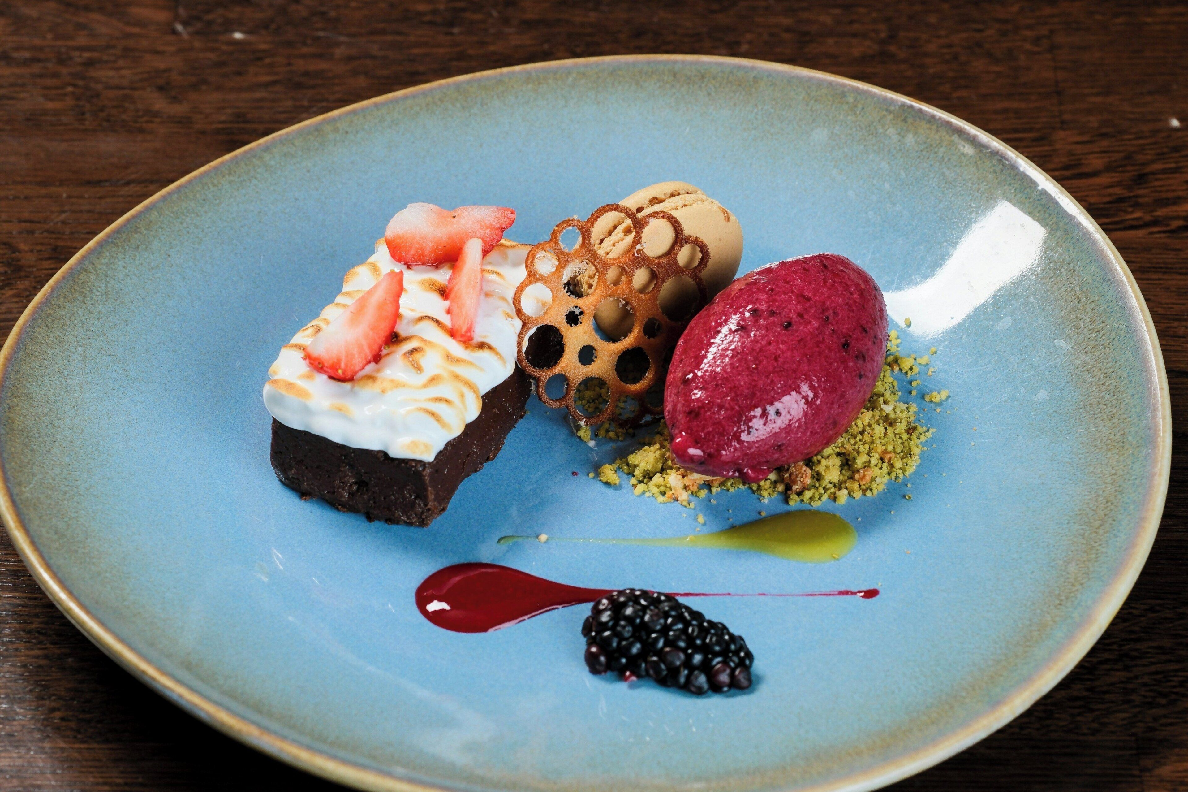 Un plato de postres con varios elementos, incluyendo un postre de chocolate, una bola de helado y una compota de frutos rojos.