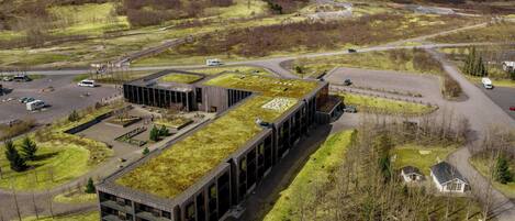 Vista aérea de un edificio moderno con techo verde, rodeado de un estacionamiento y un paisaje montañoso.