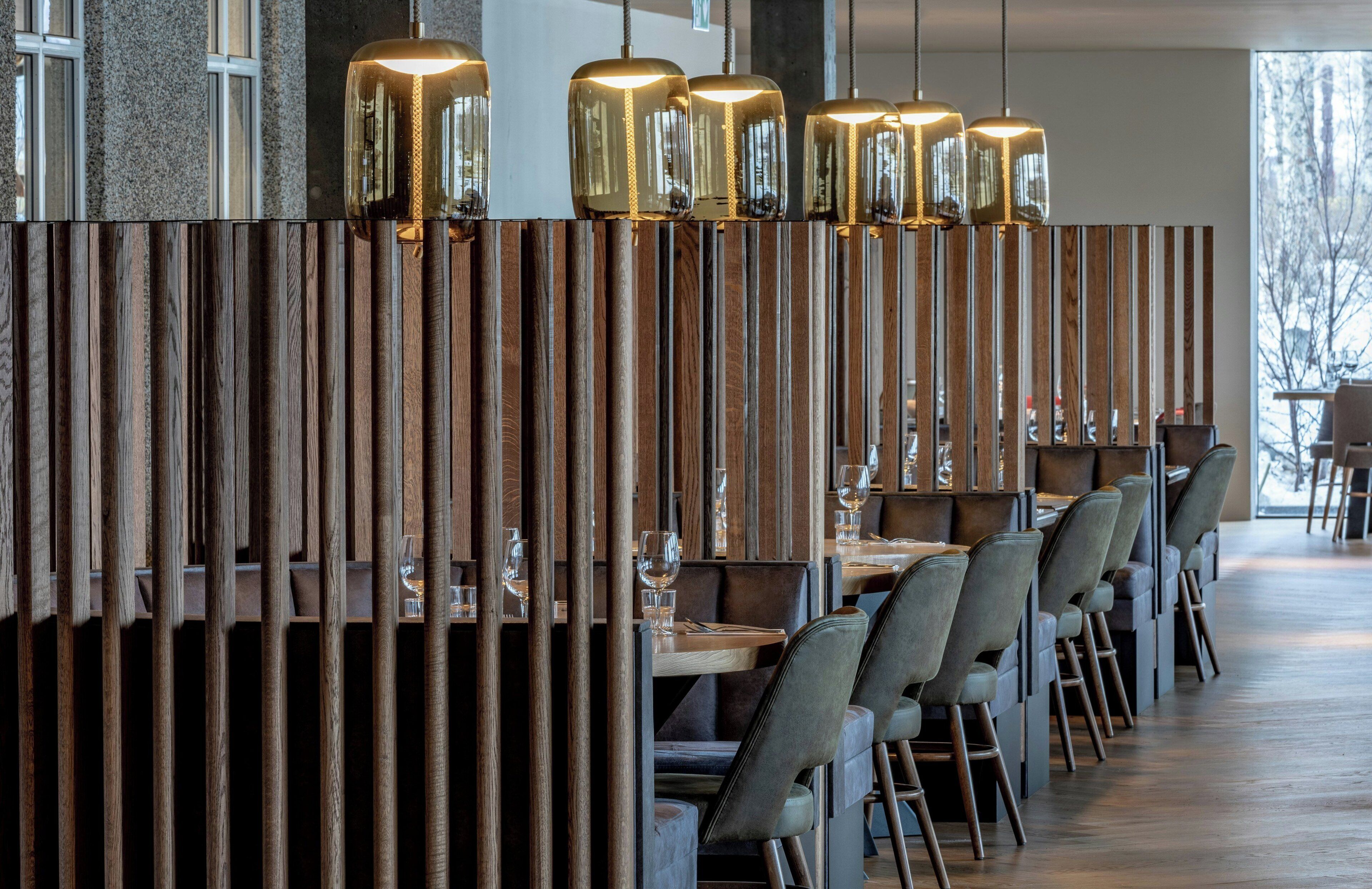 A restaurant with wooden partitions, tables, chairs, and pendant lighting.