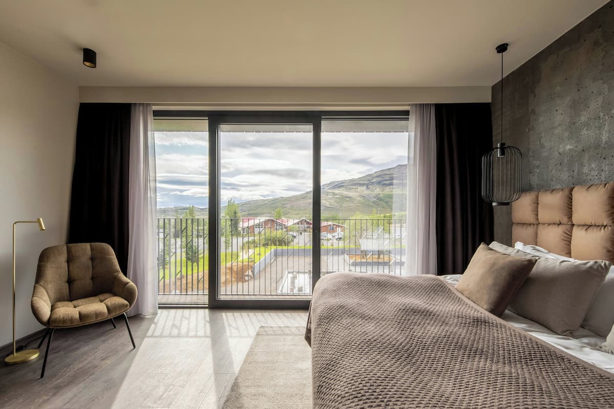 A modern bedroom with a large sliding glass door, a sofa, a bed with a headboard, and a floor lamp.