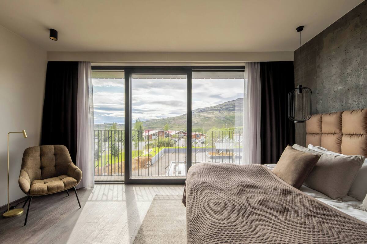 A modern bedroom with a large sliding glass door, a sofa, a bed with a headboard, and a floor lamp.