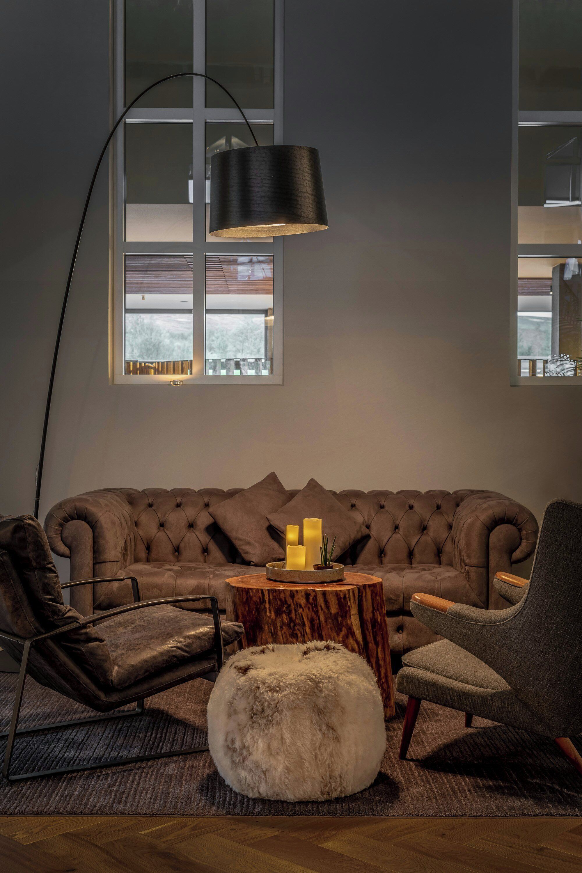 A modern living room with a tufted sofa, a round wooden coffee table, a floor lamp, and a large window.