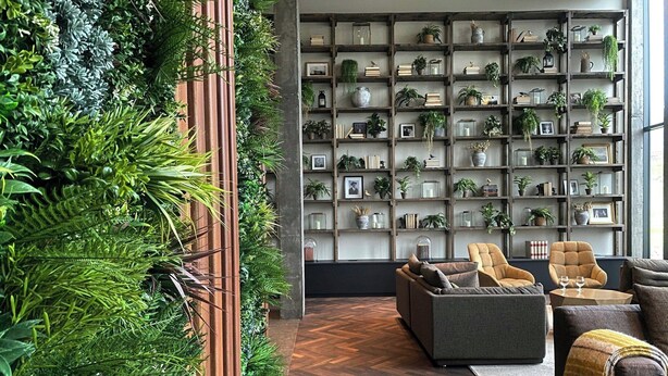 A modern living room with a herringbone wood floor, a grey sofa, two armchairs, a coffee table, and a large bookshelf filled with plants and books. - Hotel Geysir (Bláskógabyggd)