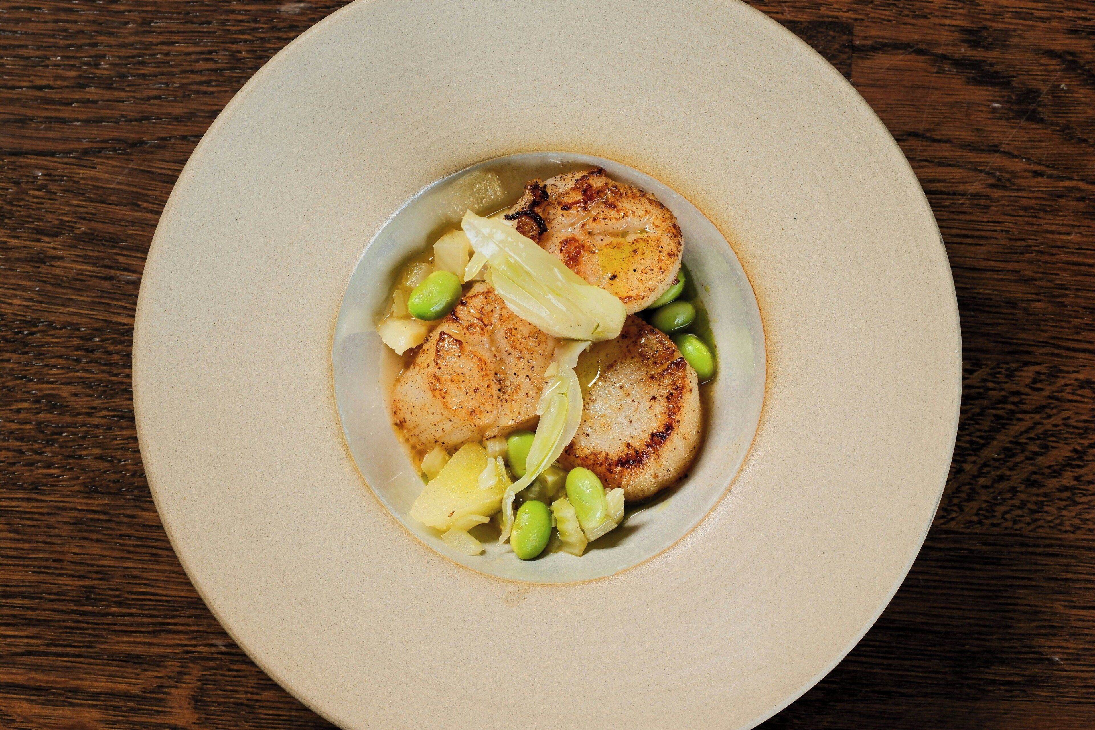 A plate with seared scallops, green beans, and a small portion of potatoes.
