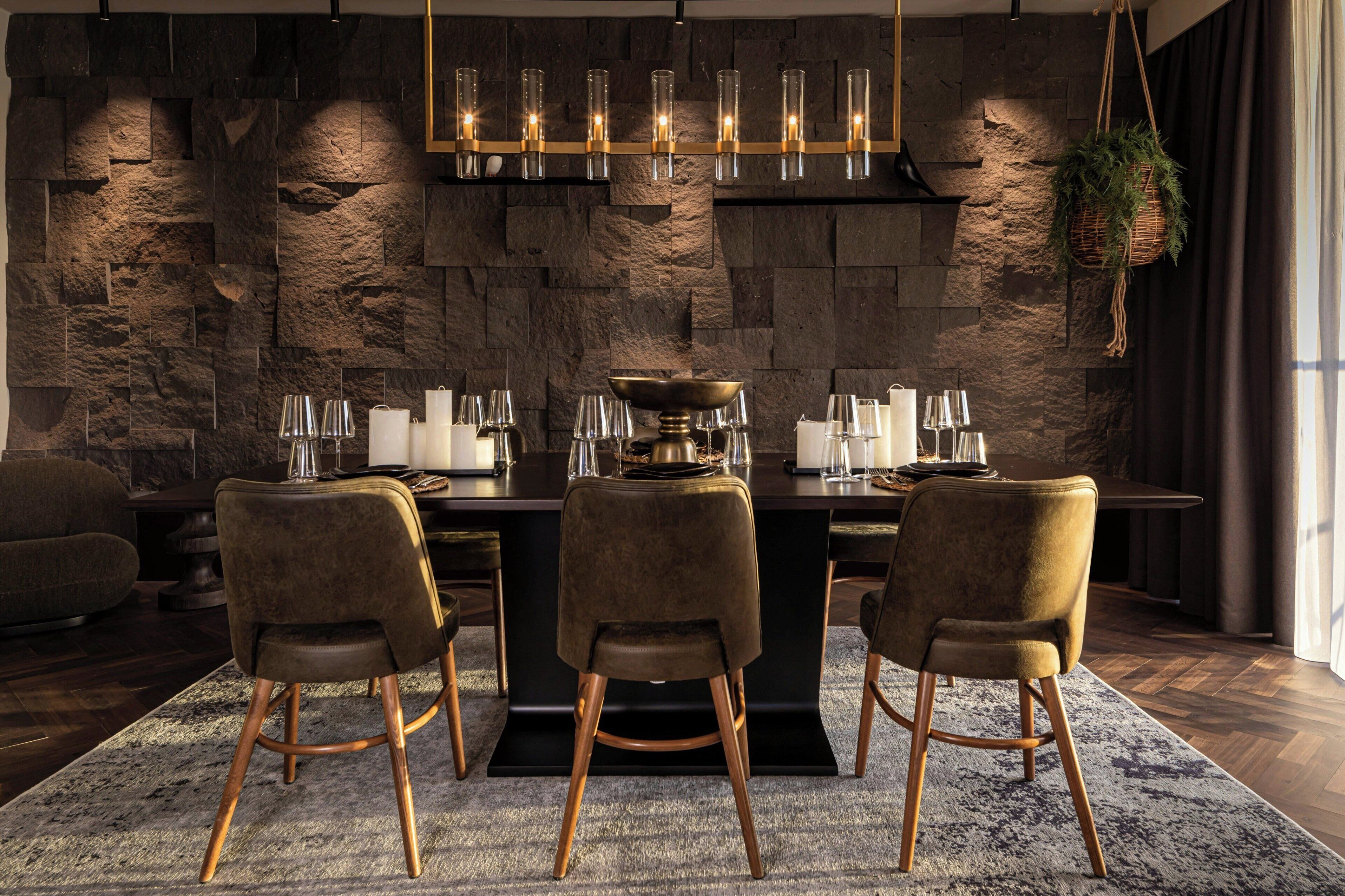 A modern dining area with a stone wall backdrop, a chandelier, and a central island with a bowl.
