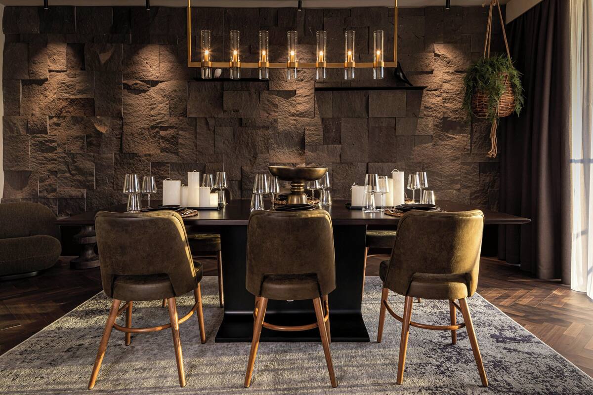 A modern dining area with a stone wall backdrop, a chandelier, and a central island with a bowl.