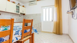 Una cocina compacta con armarios blancos, una mesa de comedor de madera con mantel azul y blanco, y un televisor montado en la pared.