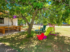 Children can play on the swing set and slide surrounded by lush trees and a grassy area.