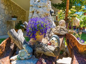 Stroll through a serene garden oasis, surrounded by vibrant flowers, a carved rock, and whimsical bird sculptures.