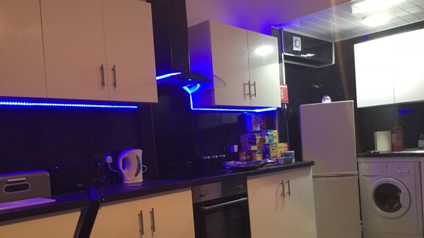A modern kitchen with white cabinets, a built-in oven, a washing machine, and blue LED lighting. - Paisley central luxury Rooms & Apartment (Paisley)