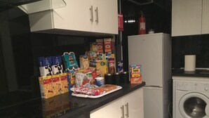 A kitchen with white cabinets, a black countertop, and a white refrigerator. There are various food items and a washing machine visible. - Paisley central luxury Rooms & Apartment (Paisley)