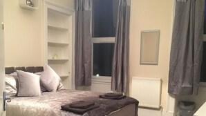 A bedroom with a bed, a nightstand, a dresser, a window with curtains, and a radiator. - Paisley central luxury Rooms & Apartment (Paisley)