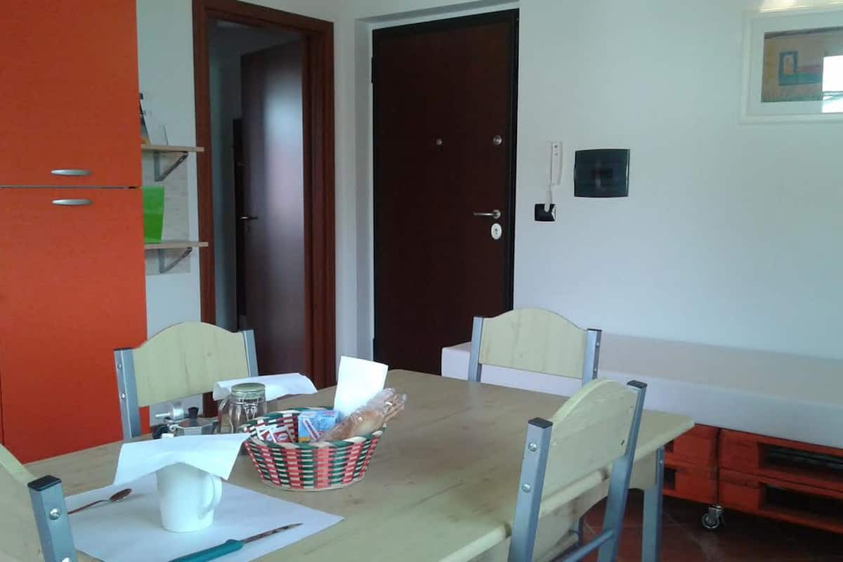 Un comedor con una mesa de madera, cuatro sillas, una cesta de pan y una taza blanca.