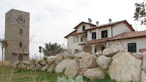 Ein steinerner Turm und ein weißes Haus mit Ziegeldach, umgeben von großen Steinen und Vegetation.