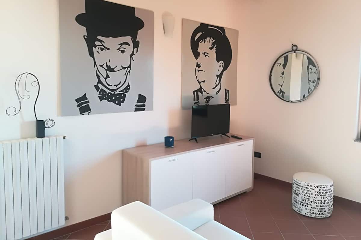 Una sala de estar moderna con un sofá blanco, un televisor sobre un mueble blanco, y dos obras de arte blanco y negro en la pared.