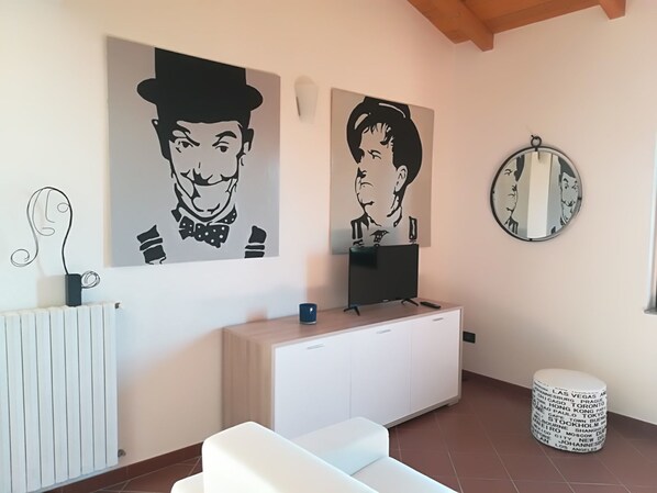 Un salon moderne avec un canapé blanc, un téléviseur posé sur un meuble blanc et deux œuvres d’art en noir et blanc accrochées au mur.