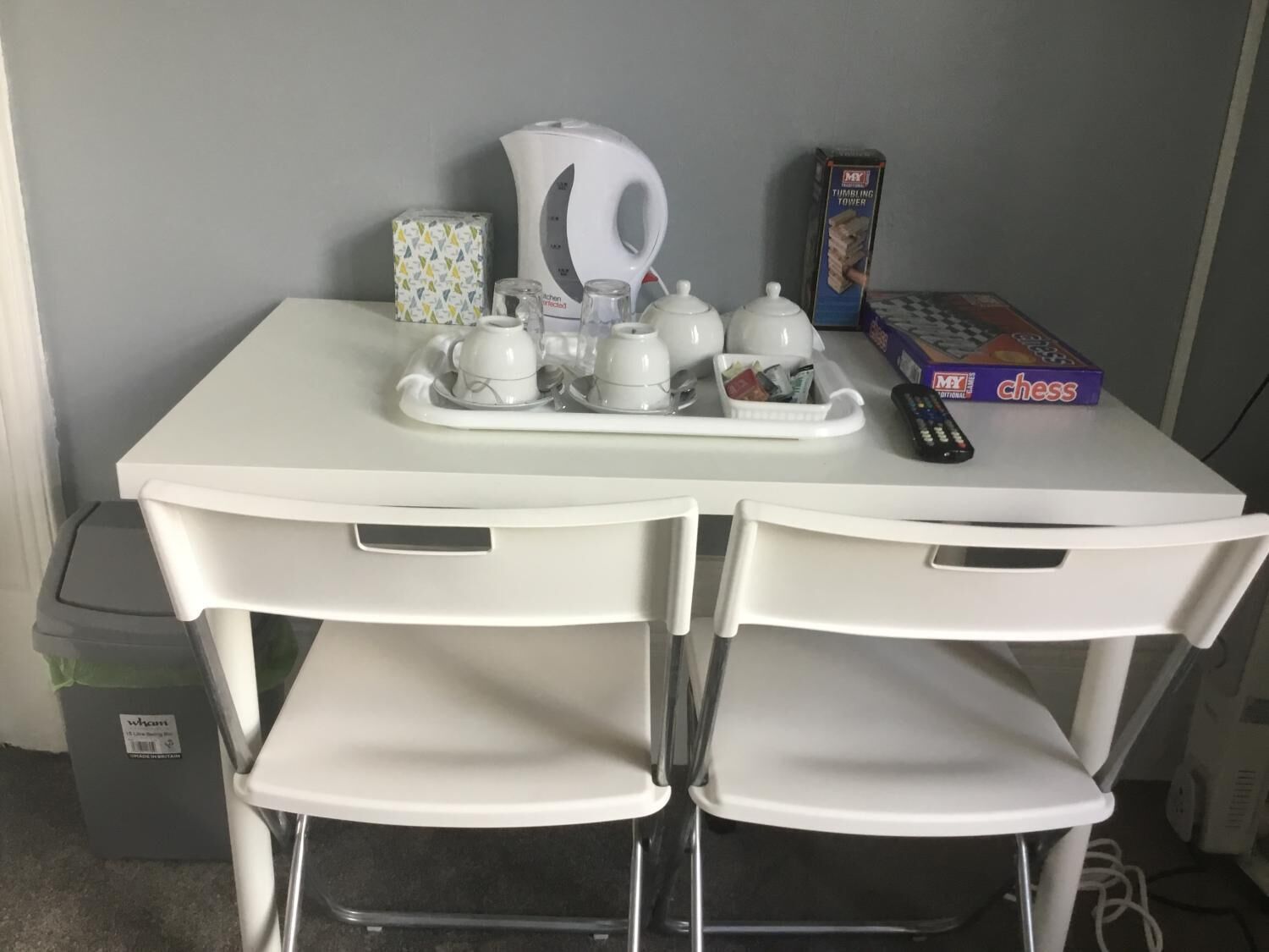 A white table with a tea set, a chess board, and a remote control.