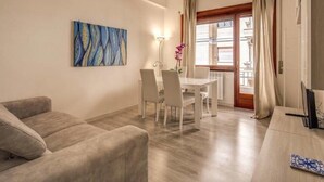 A living room with a sofa, a dining table with chairs, a painting on the wall, and a window with curtains. - Retro2 Vaticano-max 4 pax (Rome)