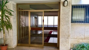 A room with a sliding glass door leading to a hallway with a red carpet. There is a potted plant on the left and another on the right. - Retro2 Vaticano-max 4 pax (Rome)