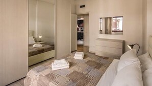 A bedroom with a bed, a bedside table with a lamp, a dresser, and a mirror. - Retro2 Vaticano-max 4 pax (Rome)