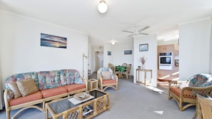 A living room with a sofa, chairs, a dining table, and a kitchen area with an oven. - Sundial 602, Hollingworth Street (Port Macquarie)