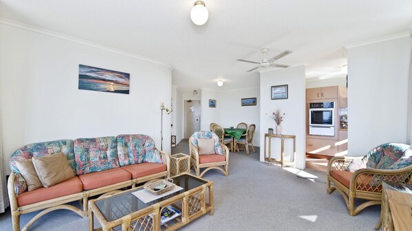 A living room with a sofa, chairs, a dining table, and a kitchen area with an oven.