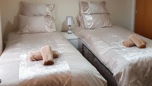 Ein Doppelzimmer mit zwei Betten, jeweils mit einem Kissen, einem kleinen Tisch mit Lampe sowie einer Deckenleuchte.