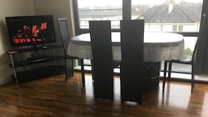 Ein Essbereich mit einem runden Tisch und Stühlen, einem Fernseher auf einem Schrank und Blick auf Gebäude durch ein Fenster.