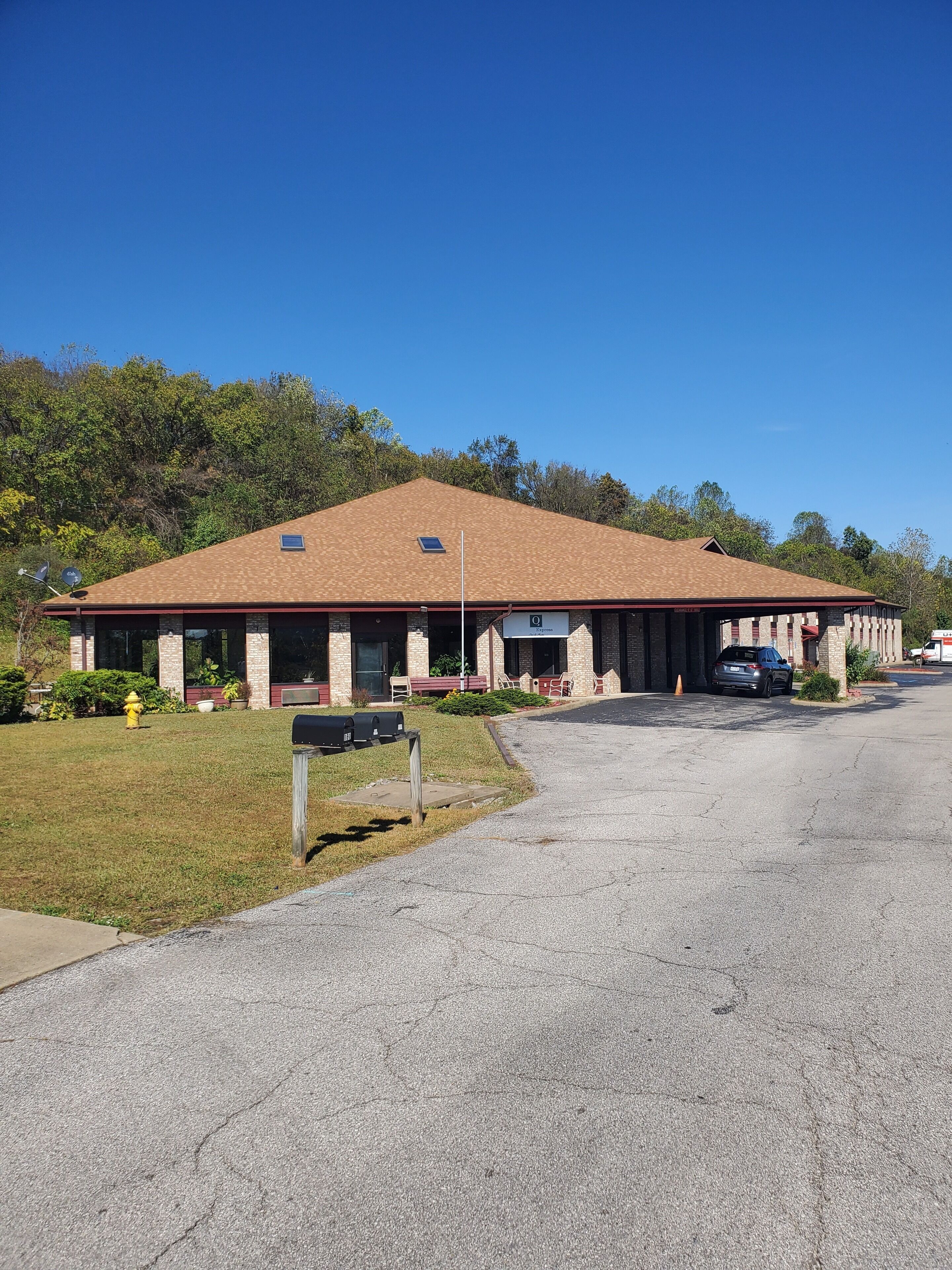 A building with a brown roof, a covered entrance, and a parking area.