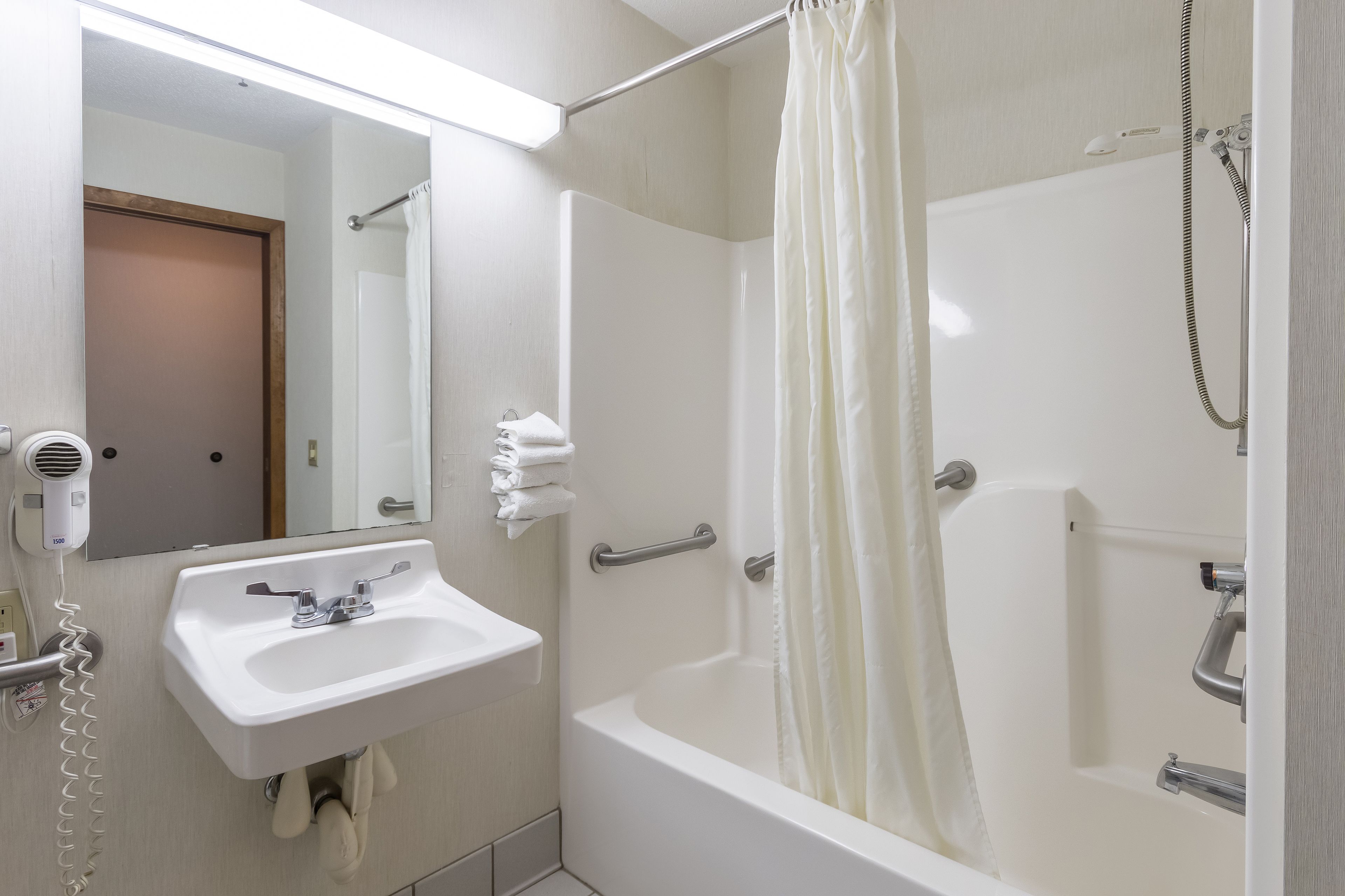 A bathroom with a white sink, a mirror, a shower with a curtain, and a door.